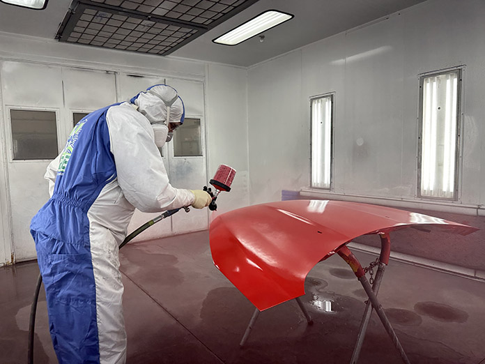 Technician spraying red panel in the Brewco spray booth, Auto Body Specialties